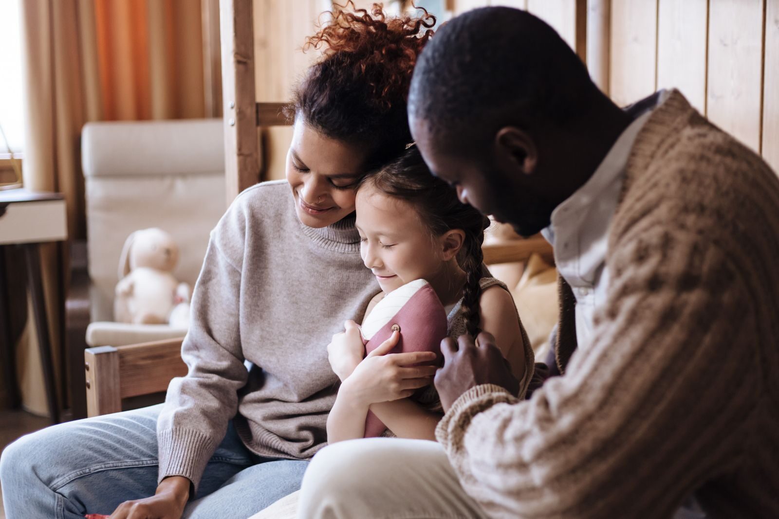 A mother and father cuddling their preschool-aged daughter