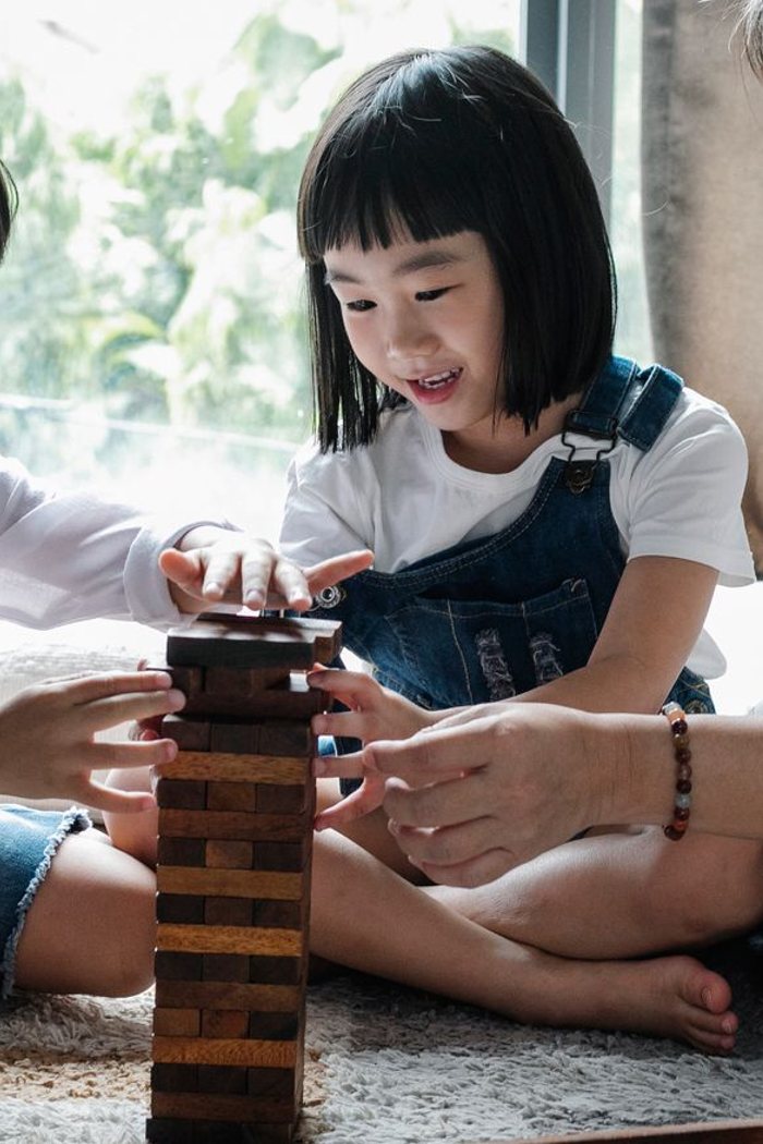 Two young children building a wooden block tower on the floor with a family member