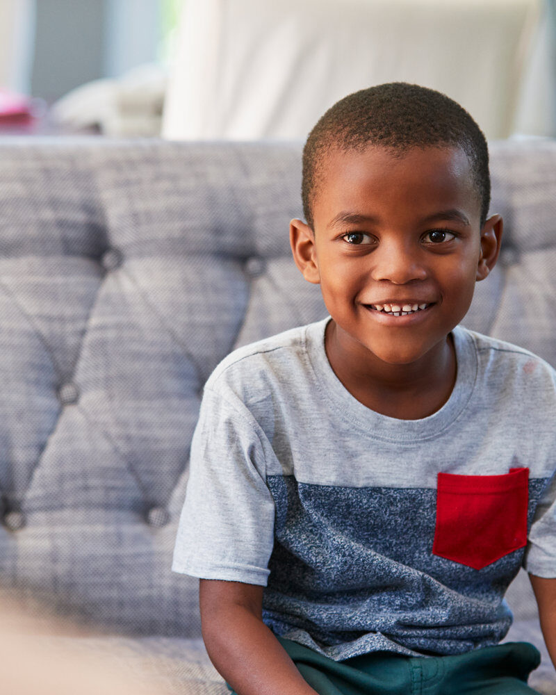 A smiling school-age boy sitting on a sofa