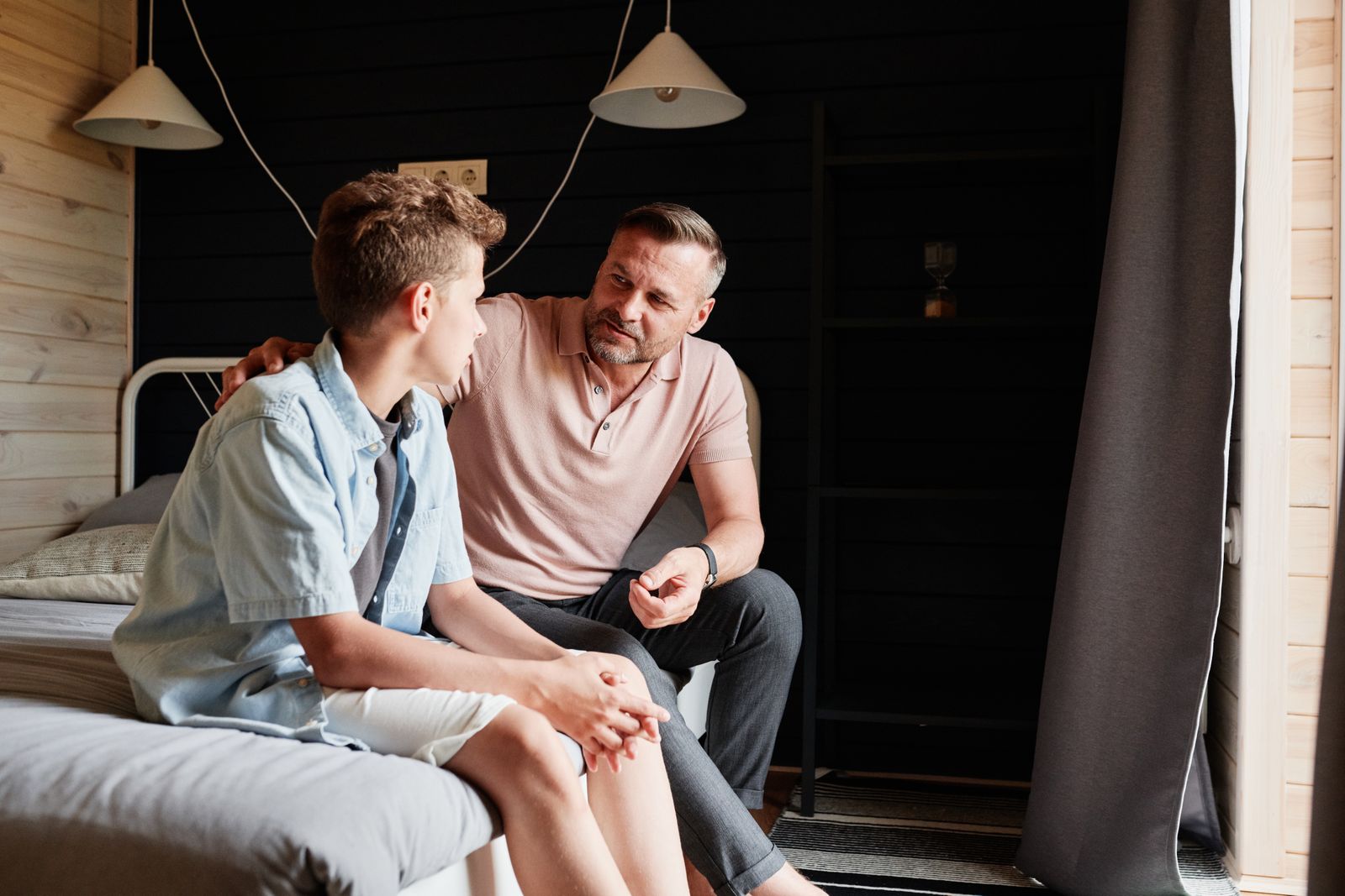 A father and his teenage son talking on a bed