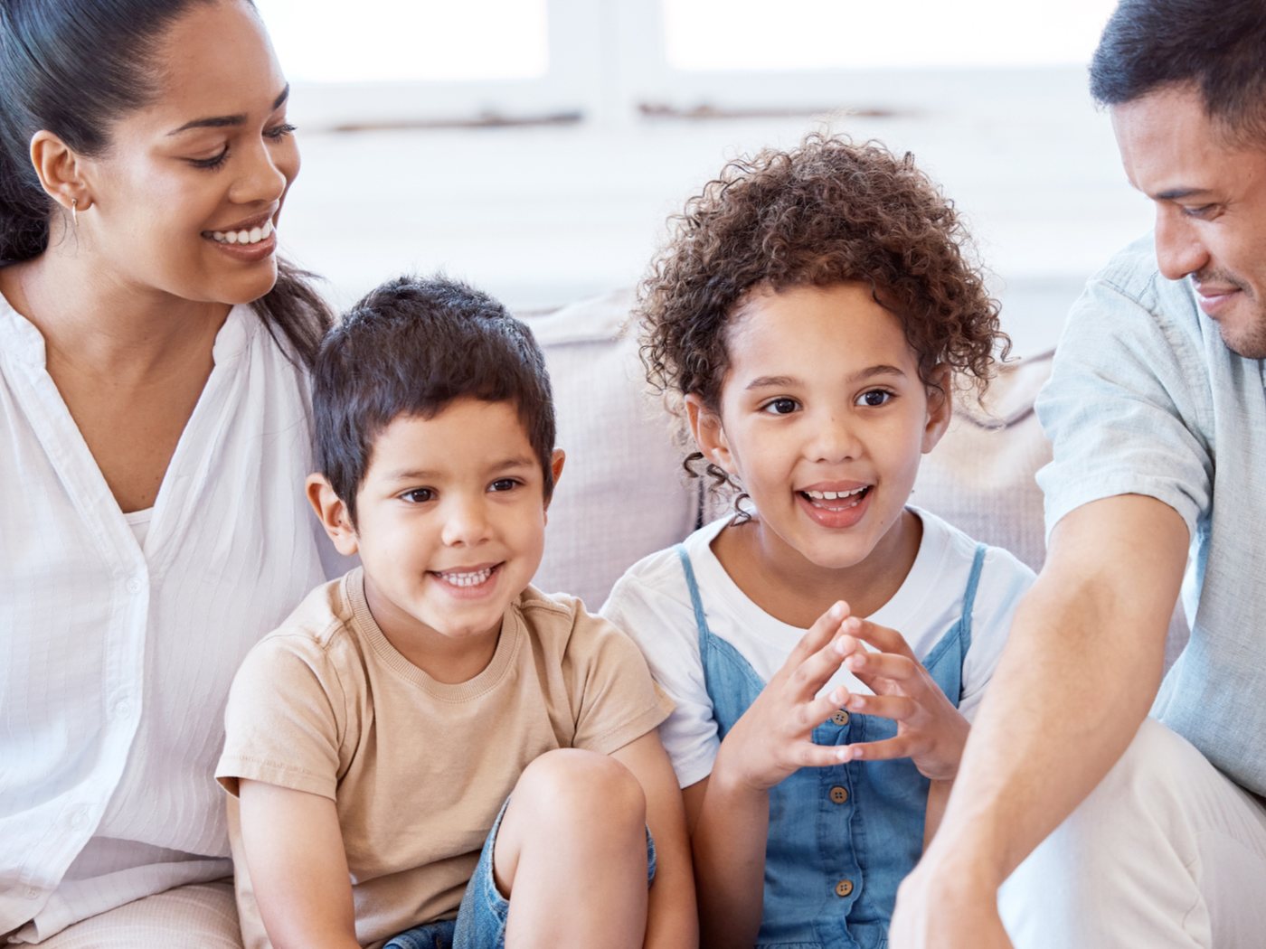 A smiling mother and father on a sofa with their young son and daughter