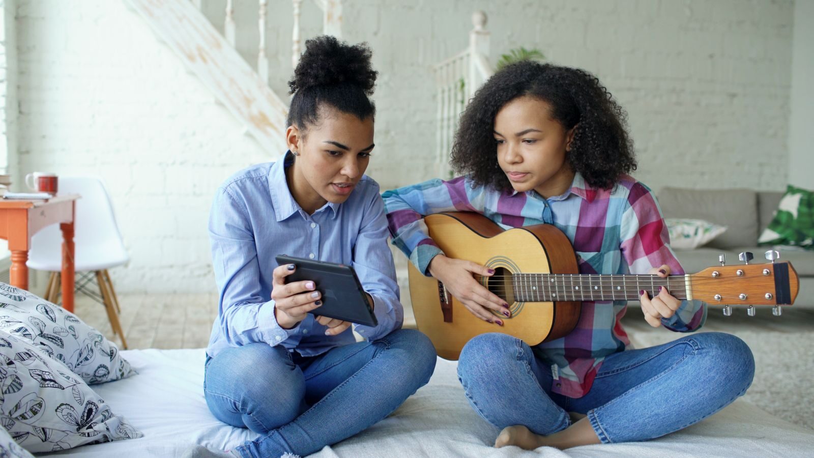 A parent and teen daughter sitting on a bed, one playing guitar