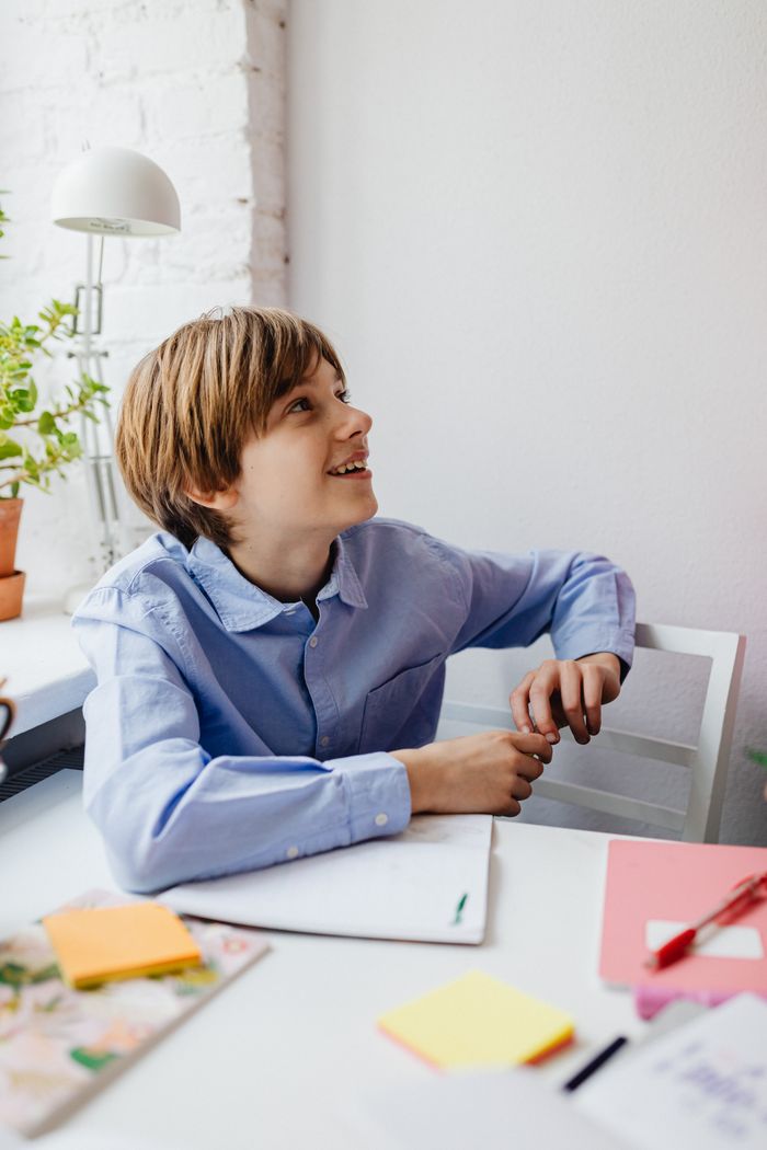 A school-age boy sitting at a desk with notebooks and sticky notes